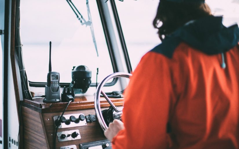Captain wearing an orange rain jacket, navigating the waters on the bridge of a vessel.