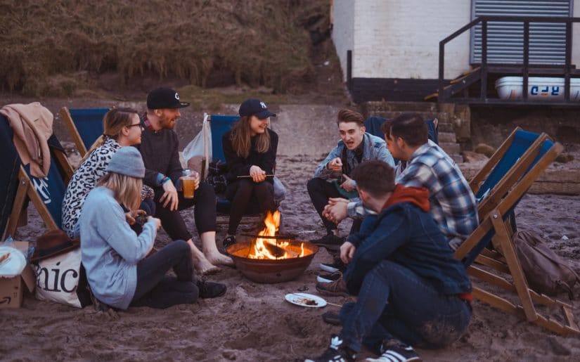 Group of young adults sitting around campfire on beach.